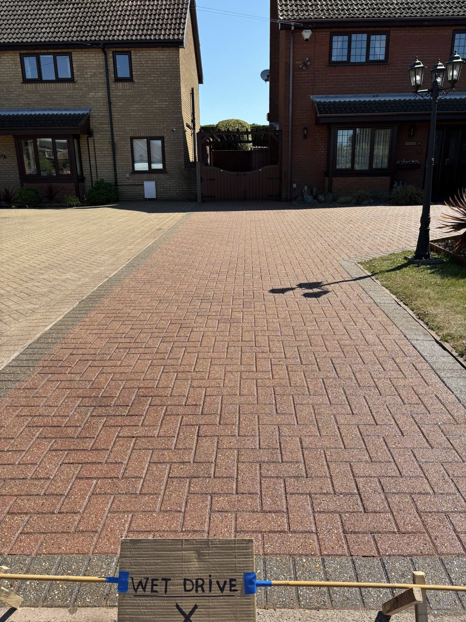 A clean, modern grey block-paved driveway with a charcoal border leading to a brick home.