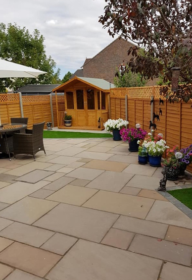 Spacious garden patio made of large, square natural stone slabs, furnished with a round dining table and chairs.